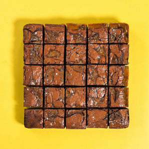 Salted Caramel Brownie by Crumbs & Doilies, fudgy squares with caramel swirls and sea salt flakes on yellow background.